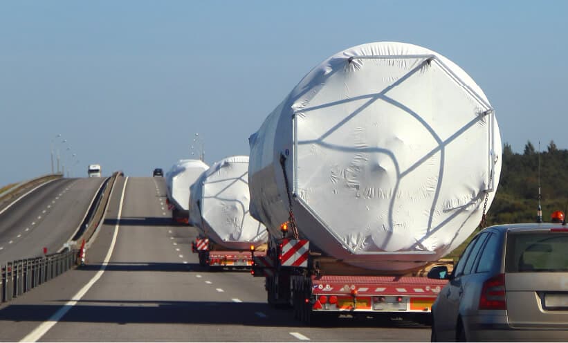 Convoy of trucks hauling wrapped oversized ring sections down a highway