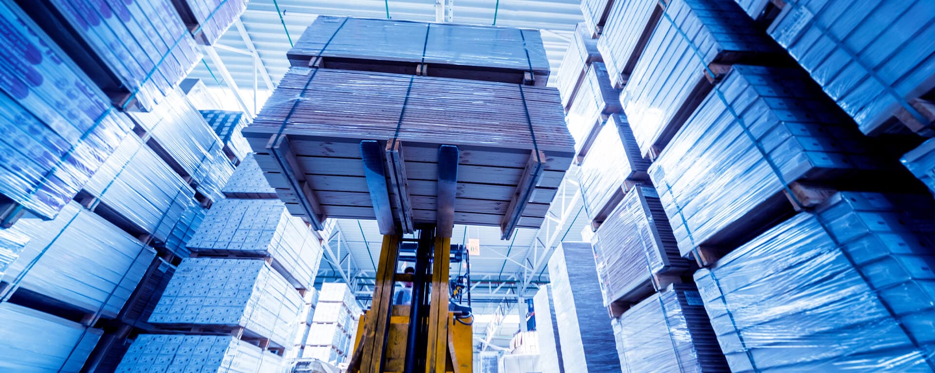 Forklift lifting heavy palletized panels inside a stacked warehouse