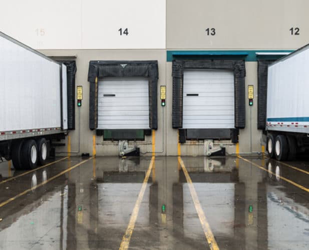 Two semi-trailers backed into numbered loading docks at a distribution center