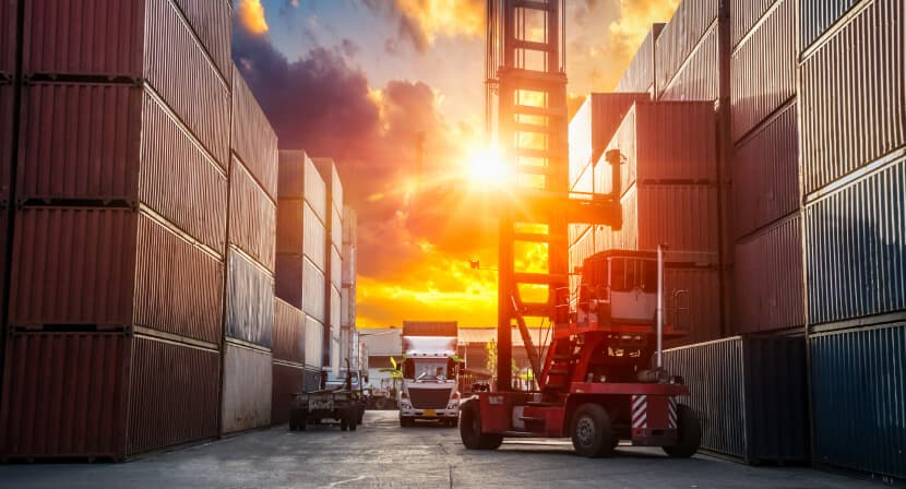Reach stacker moving containers between tall container rows at sunset