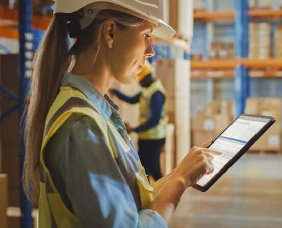 Warehouse supervisor checking inventory on a tablet beside storage racks